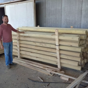 Photo d'un ouvrier se tenant près d'une palette de piquets ronds fraisés